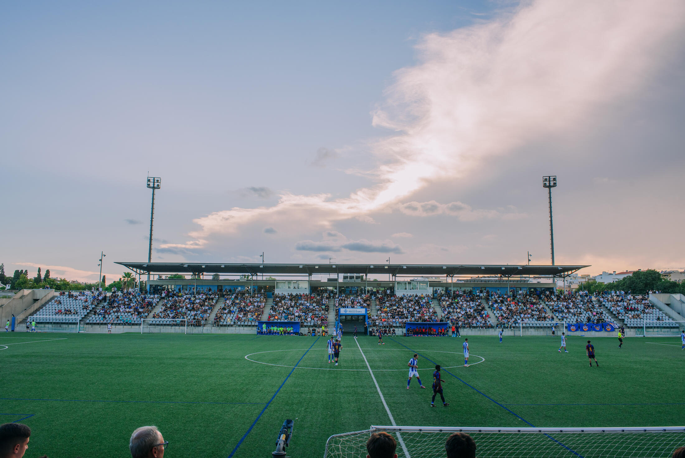 Grada llena en el Estadi Alumnes Obrers durante un partido de liga al atardecer